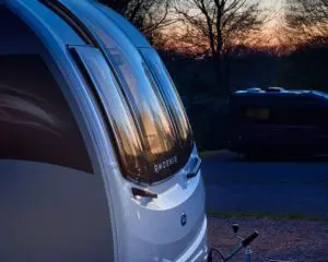 A close-up view of a Bailey caravan with reflective windows during sunset, showcasing its sleek design and countryside setting.
