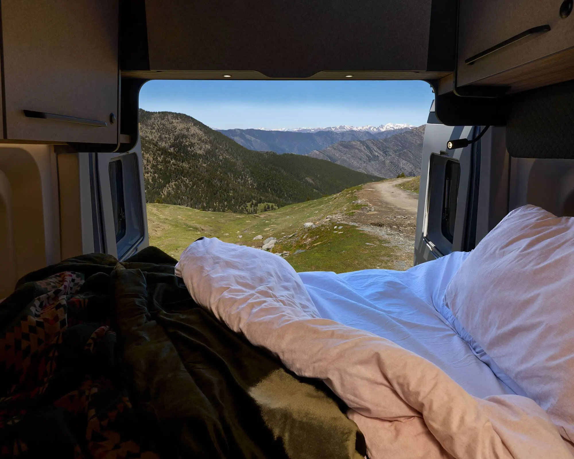 Interior view of a motorhome bed with a scenic outdoor landscape visible through the window
