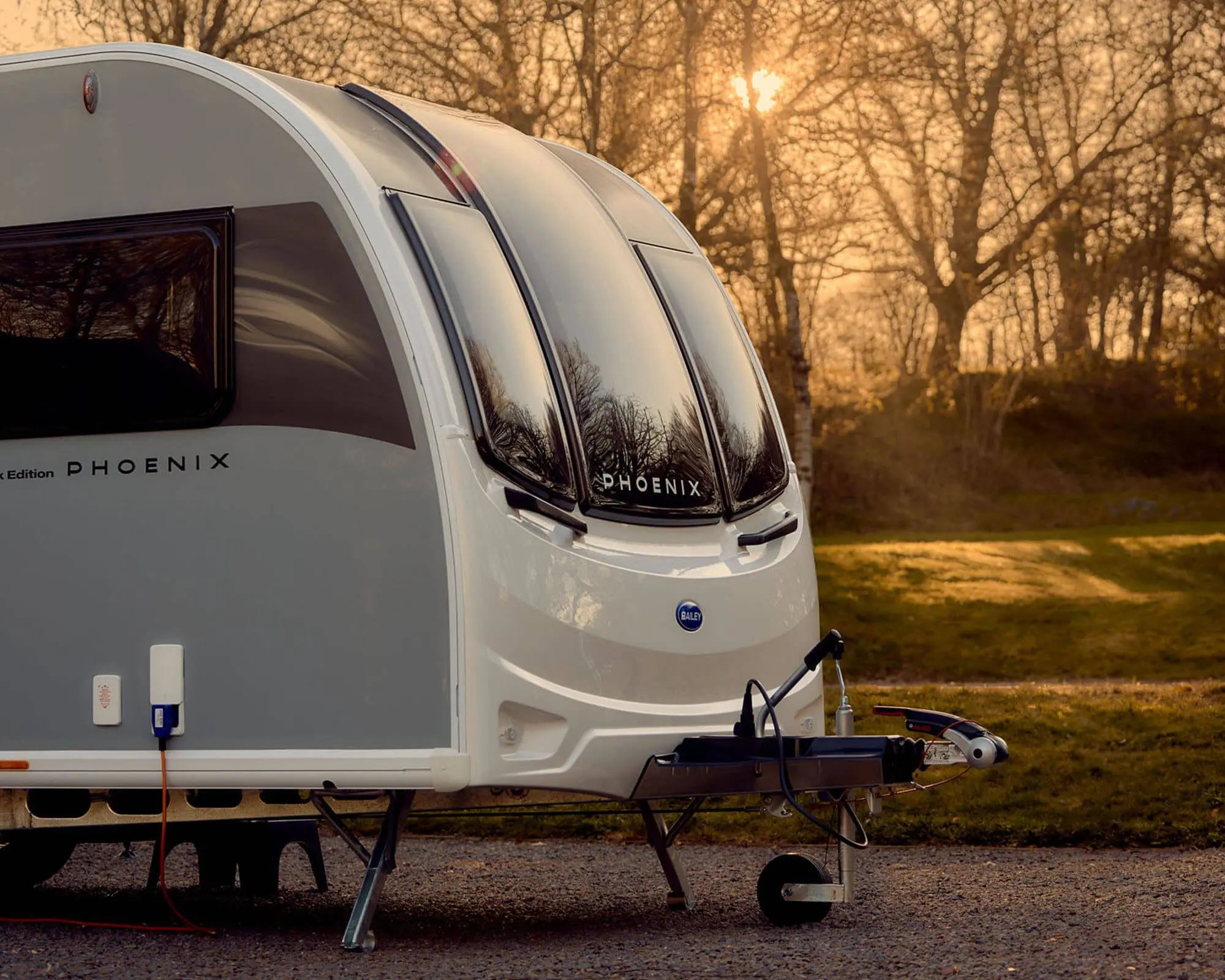 A Bailey Phoenix caravan parked in a tranquil outdoor setting at sunset.