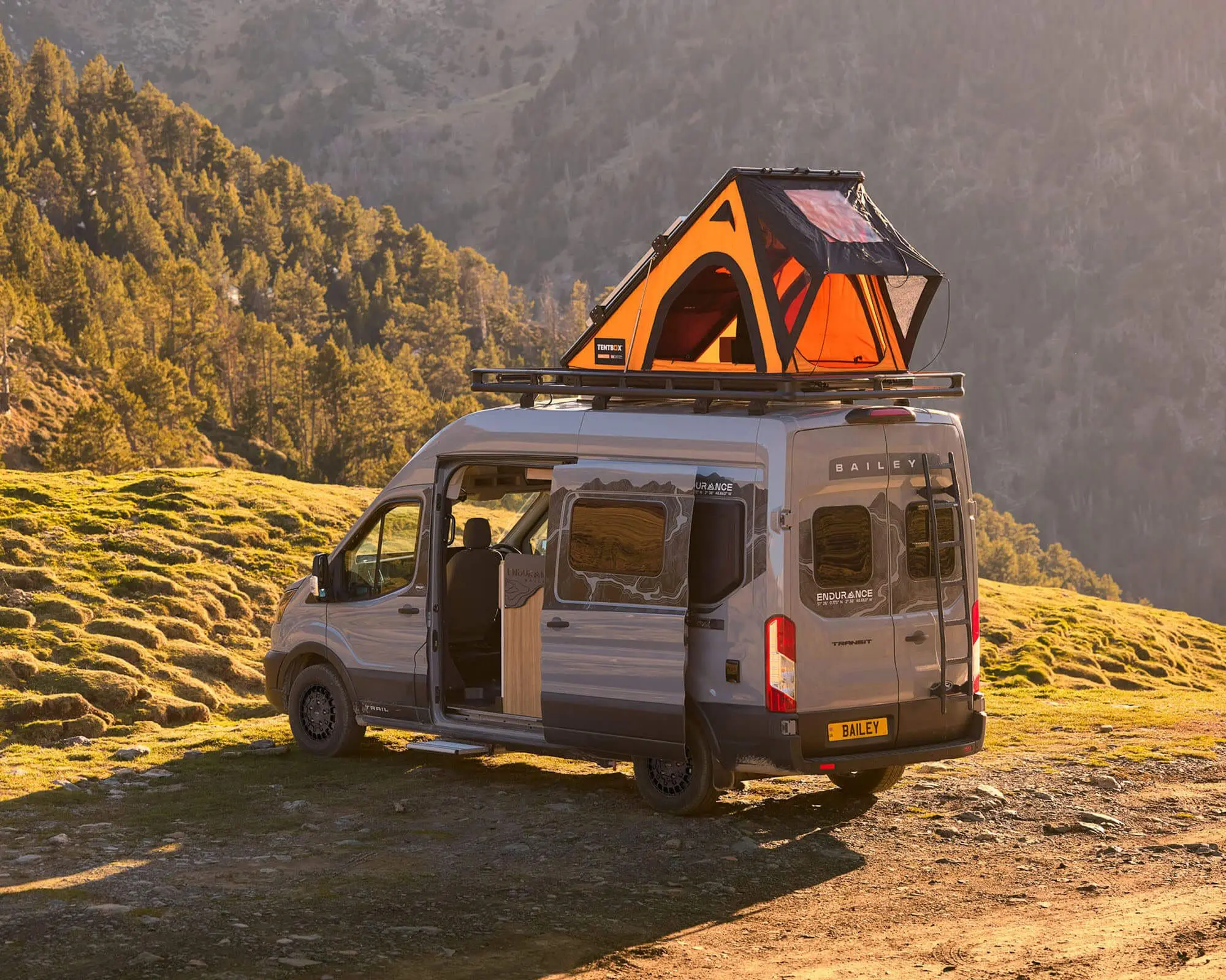 A silver Bailey campervan parked in a scenic area with a TentBox on top, showcasing outdoor adventure.