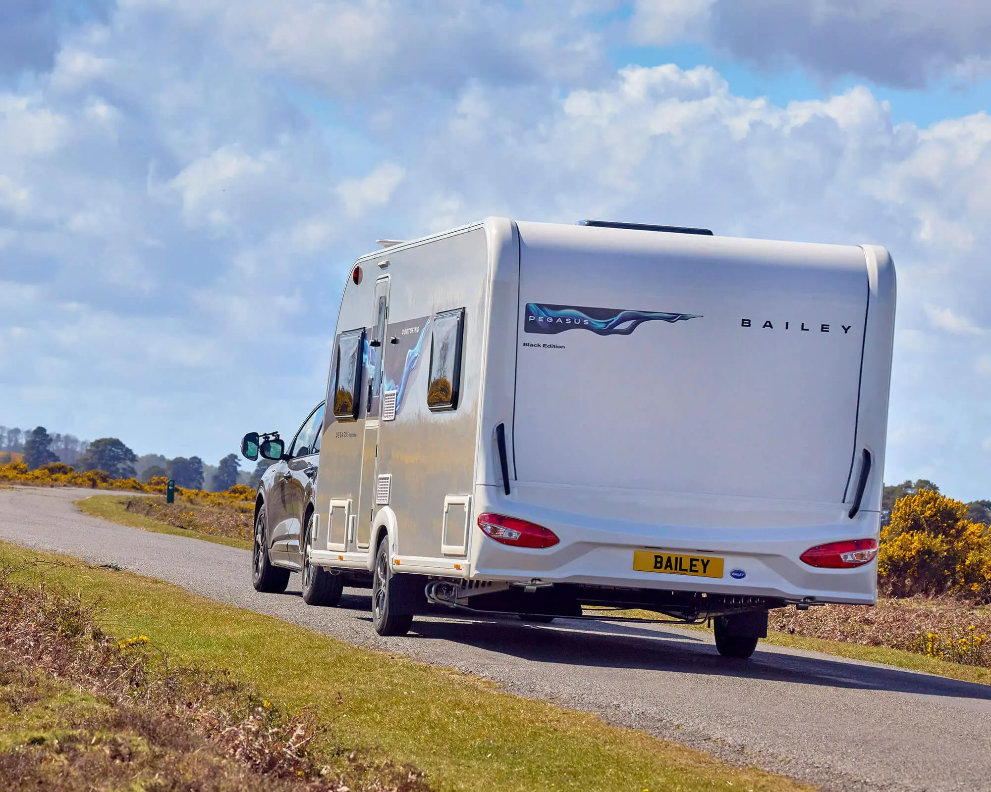 Rear view of a Bailey caravan traveling on a scenic countryside road