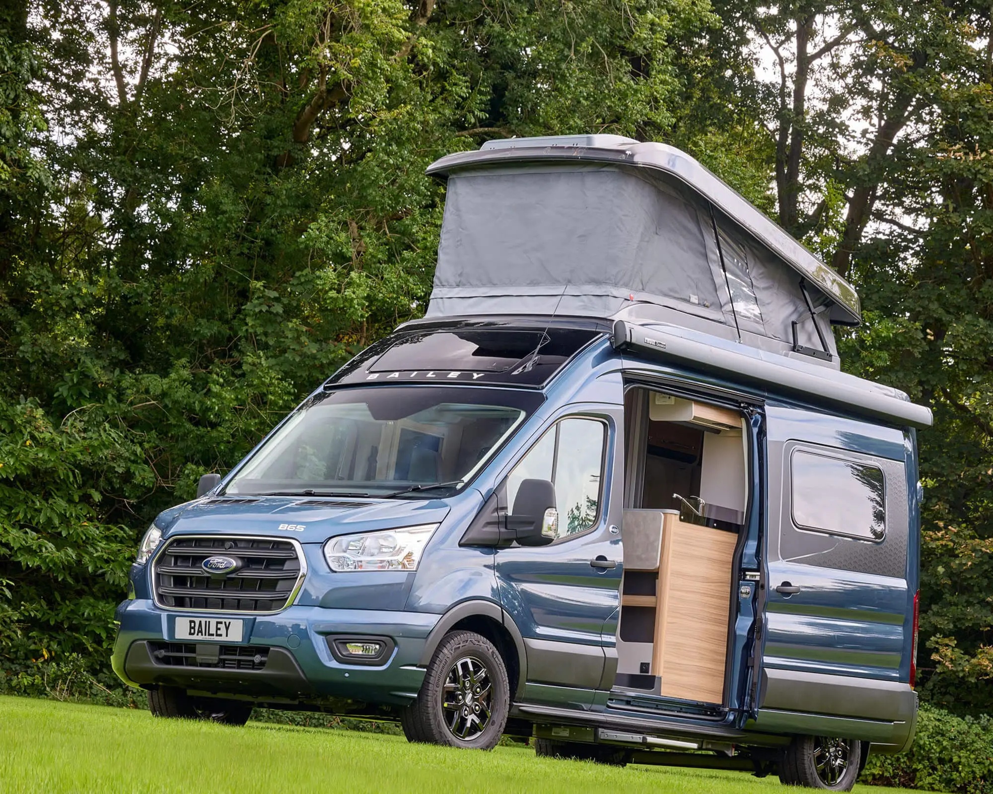 Modern blue campervan parked in a scenic outdoor setting, showcasing its pop-top roof and side entry.