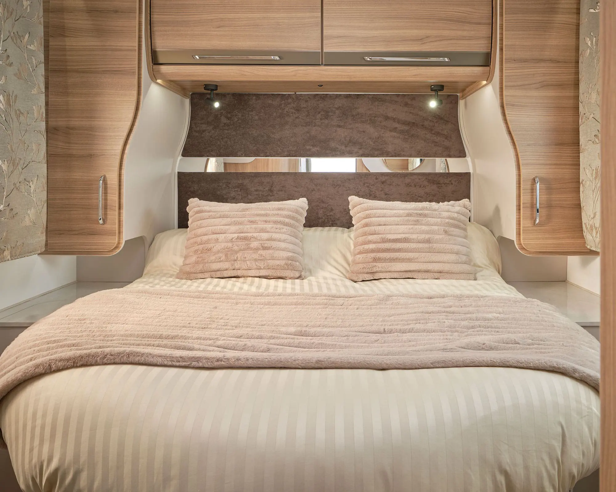 Stylish and comfortable bed setup in a Bailey motorhome with soft pillows and warm tones.