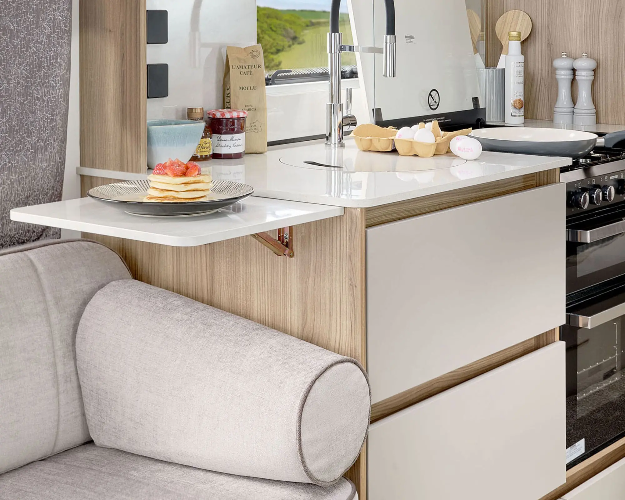 Interior view of a modern caravan kitchen featuring a dining area, sink, and storage cabinets.