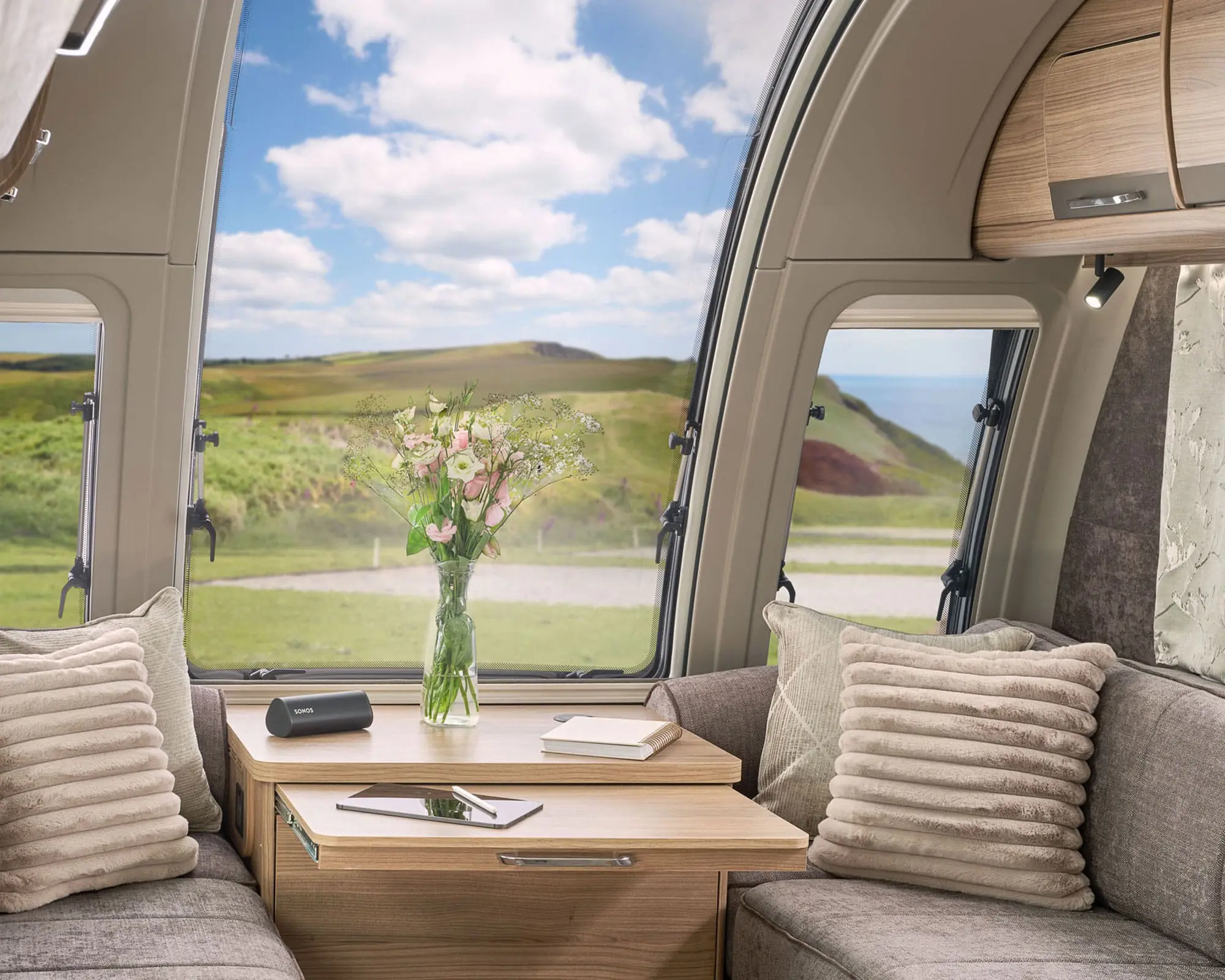 Cozy seating area inside a Bailey caravan with floral decoration and large windows showcasing outdoor scenery.