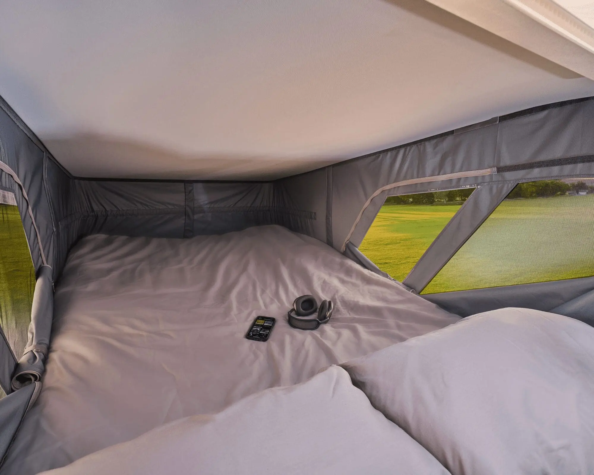 Interior view of a TentBox with bedding and windows, showcasing a comfortable sleeping area for camping on top of a vehicle.