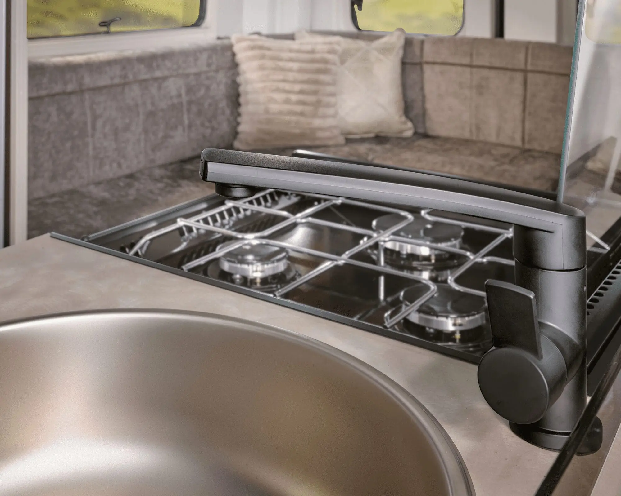 Interior view of a Bailey caravan kitchen featuring a sink and stove, with cozy seating in the background.