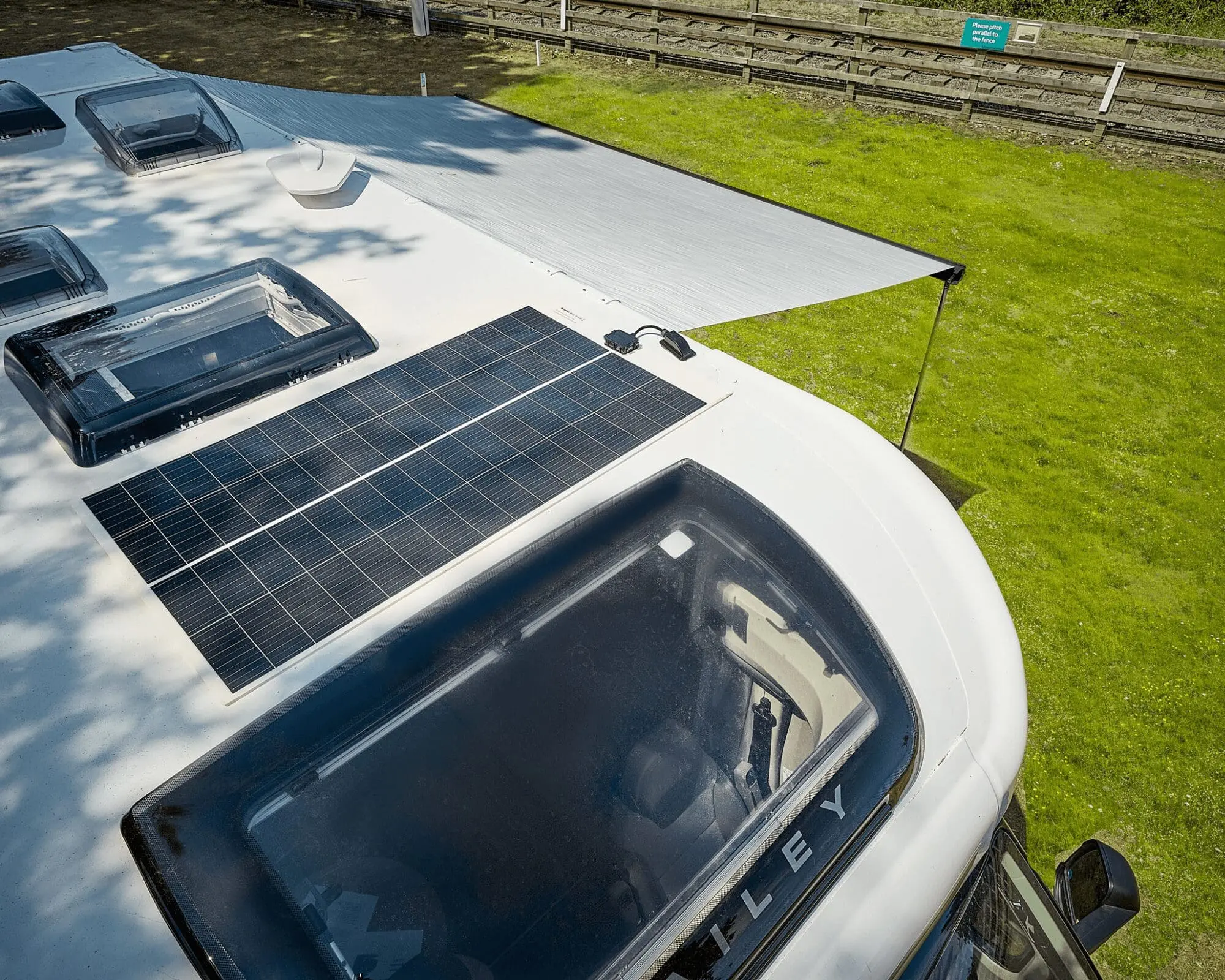 Top view of a Bailey motorhome featuring solar panels and an extended awning on a grassy area.