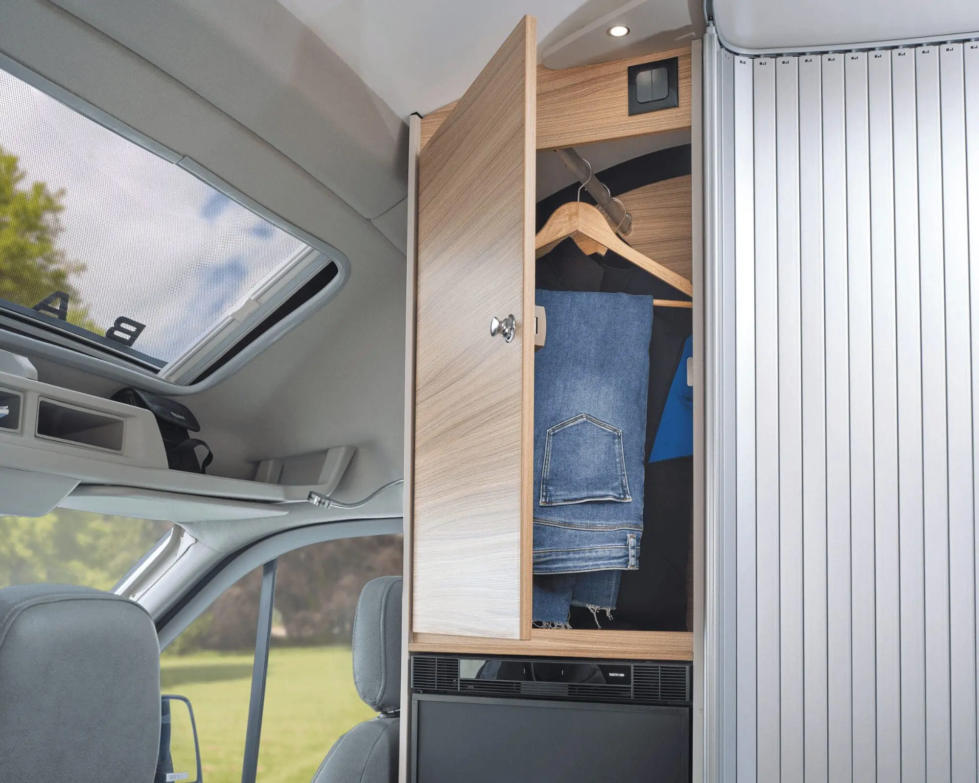A wooden cabinet inside a van, showcasing hanging clothes including jeans and a blue shirt.