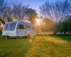 A sleek modern caravan parked in a lush green field during sunset, surrounded by trees.