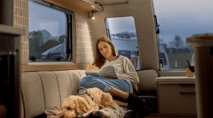 A woman sitting comfortably in a Bailey motorhome interior, reading a book with a dog on her lap, showcasing a warm and inviting space.
