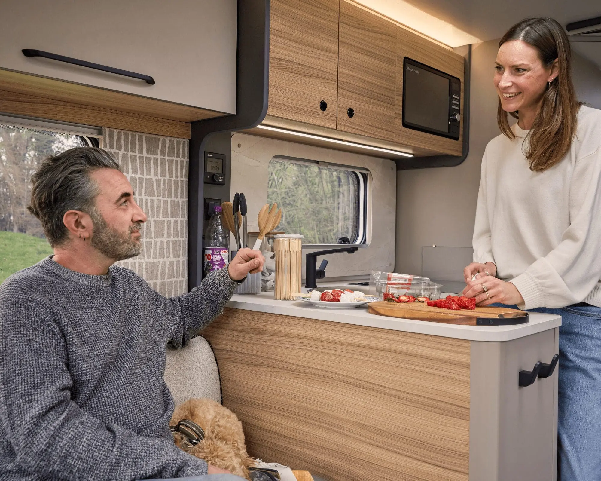A couple preparing food together inside a stylish motorhome kitchen, showcasing the spacious interior and modern design.