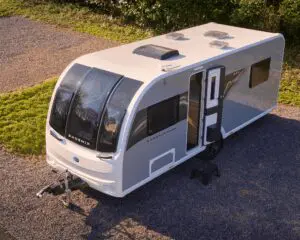 Aerial view of a stylish white caravan with large windows parked on gravel surrounded by greenery.