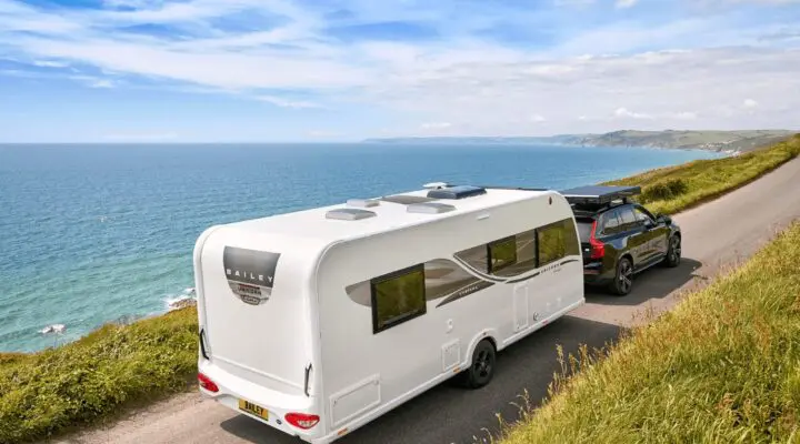 White Bailey caravan being towed along a scenic coastal road with lush greenery and sea views