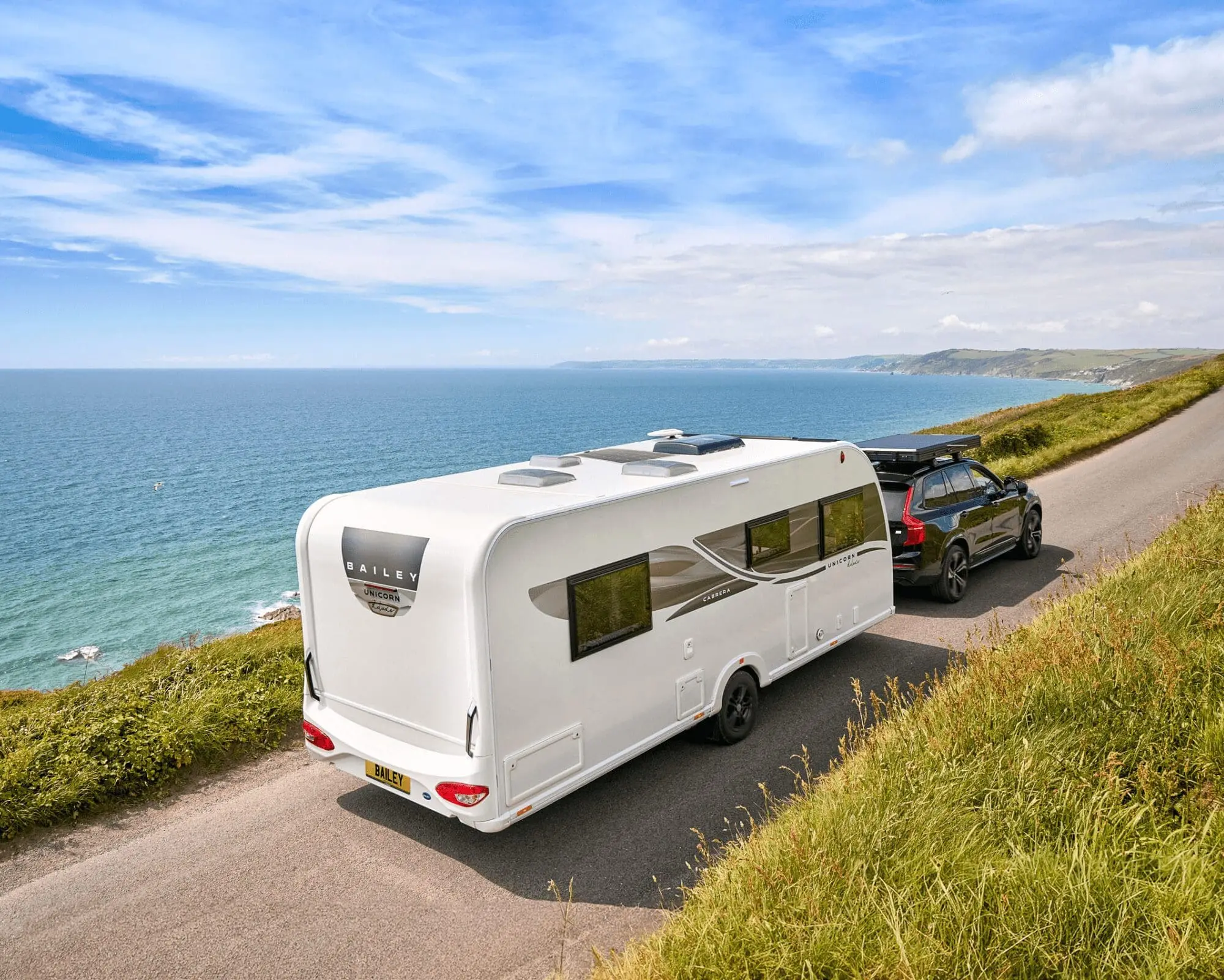 White Bailey caravan being towed along a scenic coastal road with lush greenery and sea views