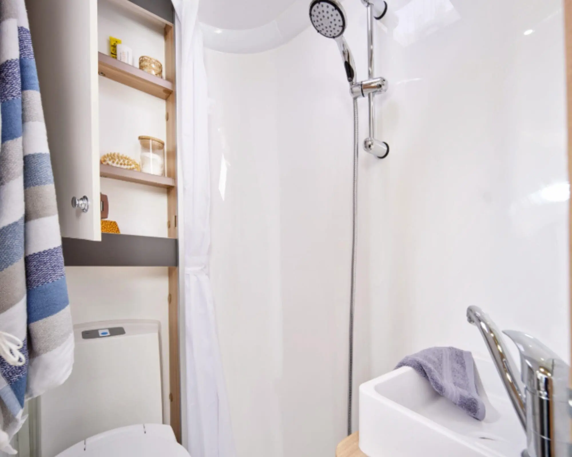 Compact Caravan Shower Room Featuring Modern Fixtures Interior view of a compact shower room in a caravan, showcasing a shower, sink, and storage shelves.
