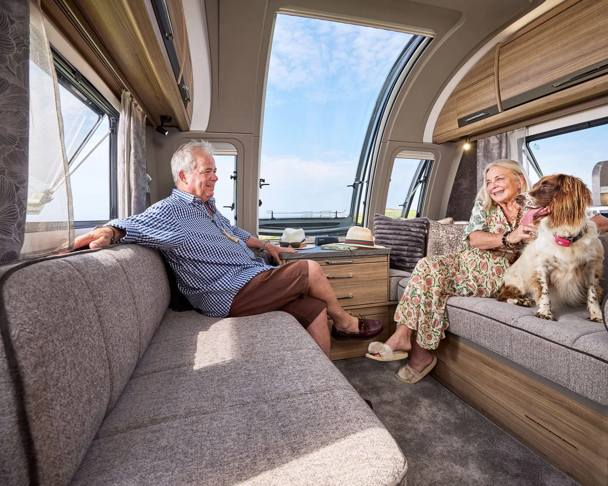 Cozy Interior of a Bailey Caravan with a Couple and Their Dog Interior view of a Bailey caravan featuring a couple relaxing on a sofa with their dog, showcasing a spacious and comfortable living area.