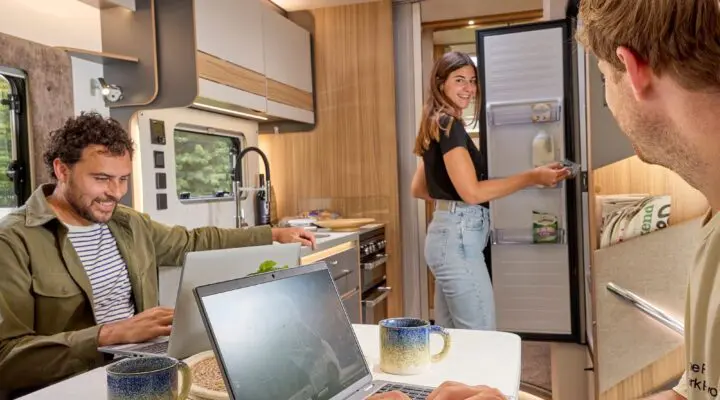 Interior view of a Bailey motorhome featuring three friends enjoying their time together, working on laptops, and looking relaxed.