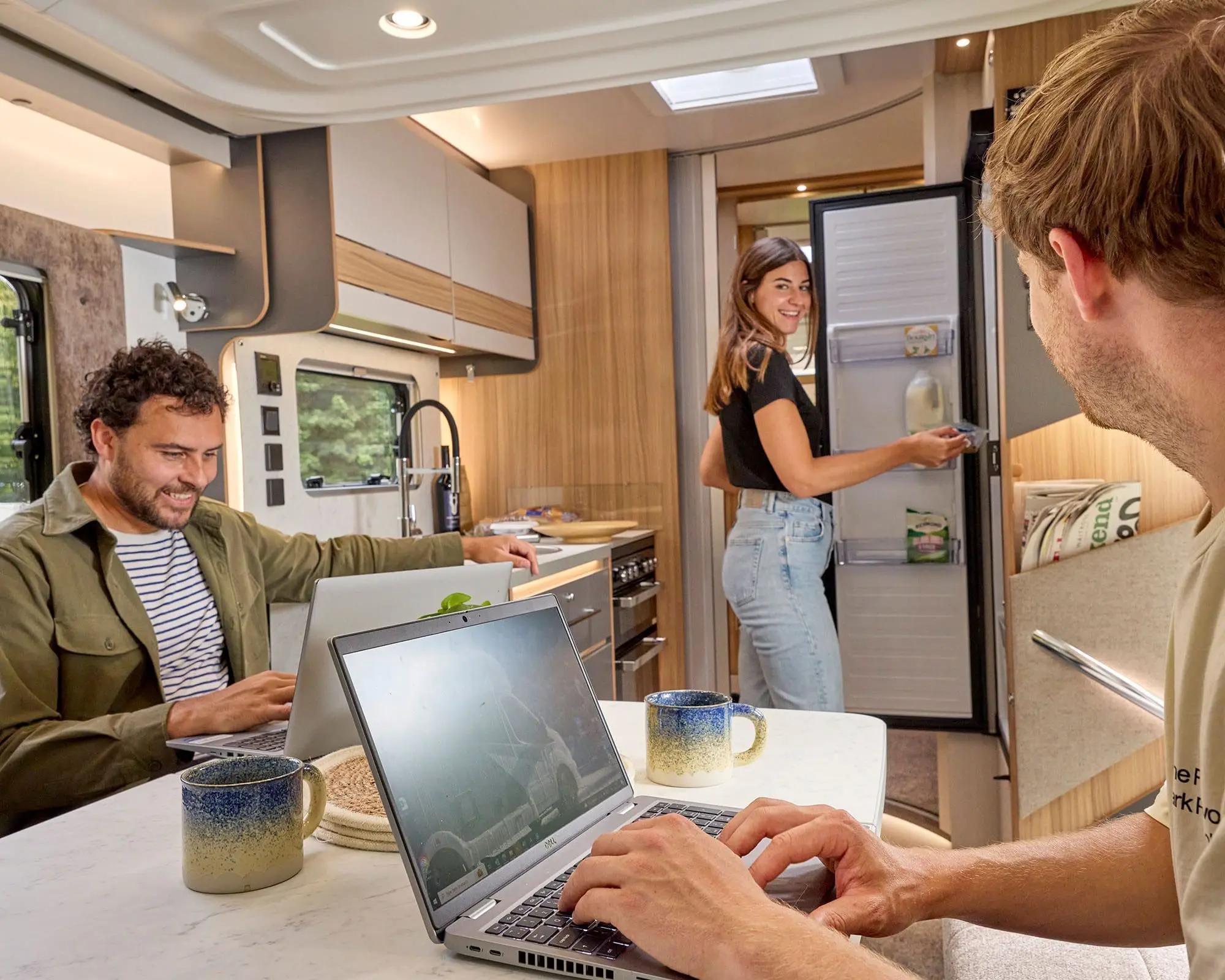 Interior view of a Bailey motorhome featuring three friends enjoying their time together, working on laptops, and looking relaxed.