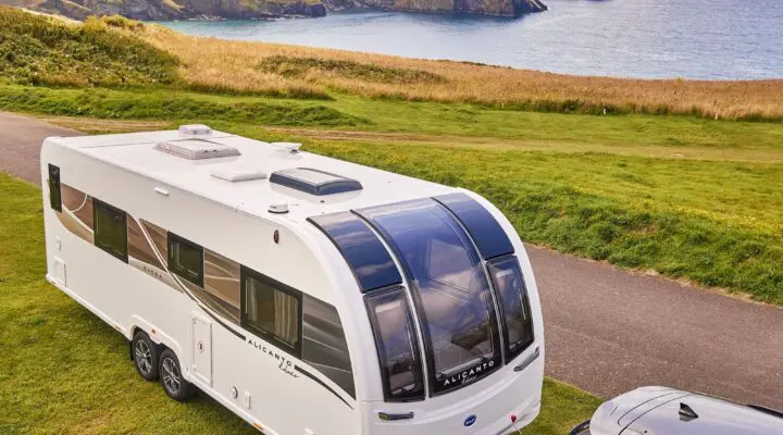 A Bailey caravan parked on green grass with a scenic coastal view in the background.
