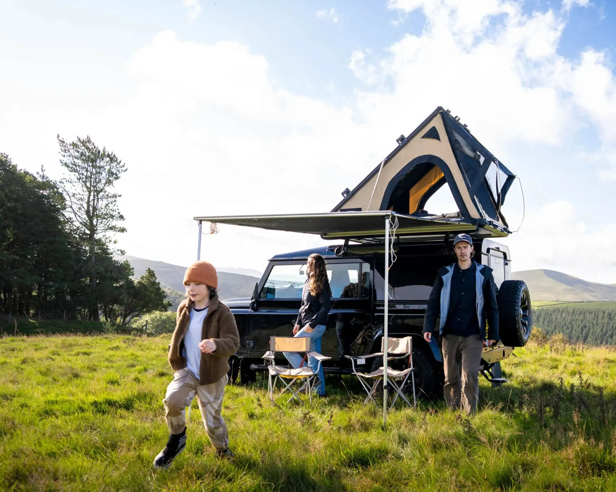 A family in a scenic outdoor setting, featuring a vehicle equipped with a TentBox, enjoying their time together in the countryside.