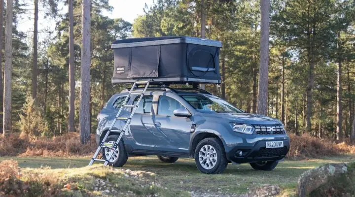 Outdoor scene featuring a gray SUV equipped with a rooftop tent parked on a forested trail