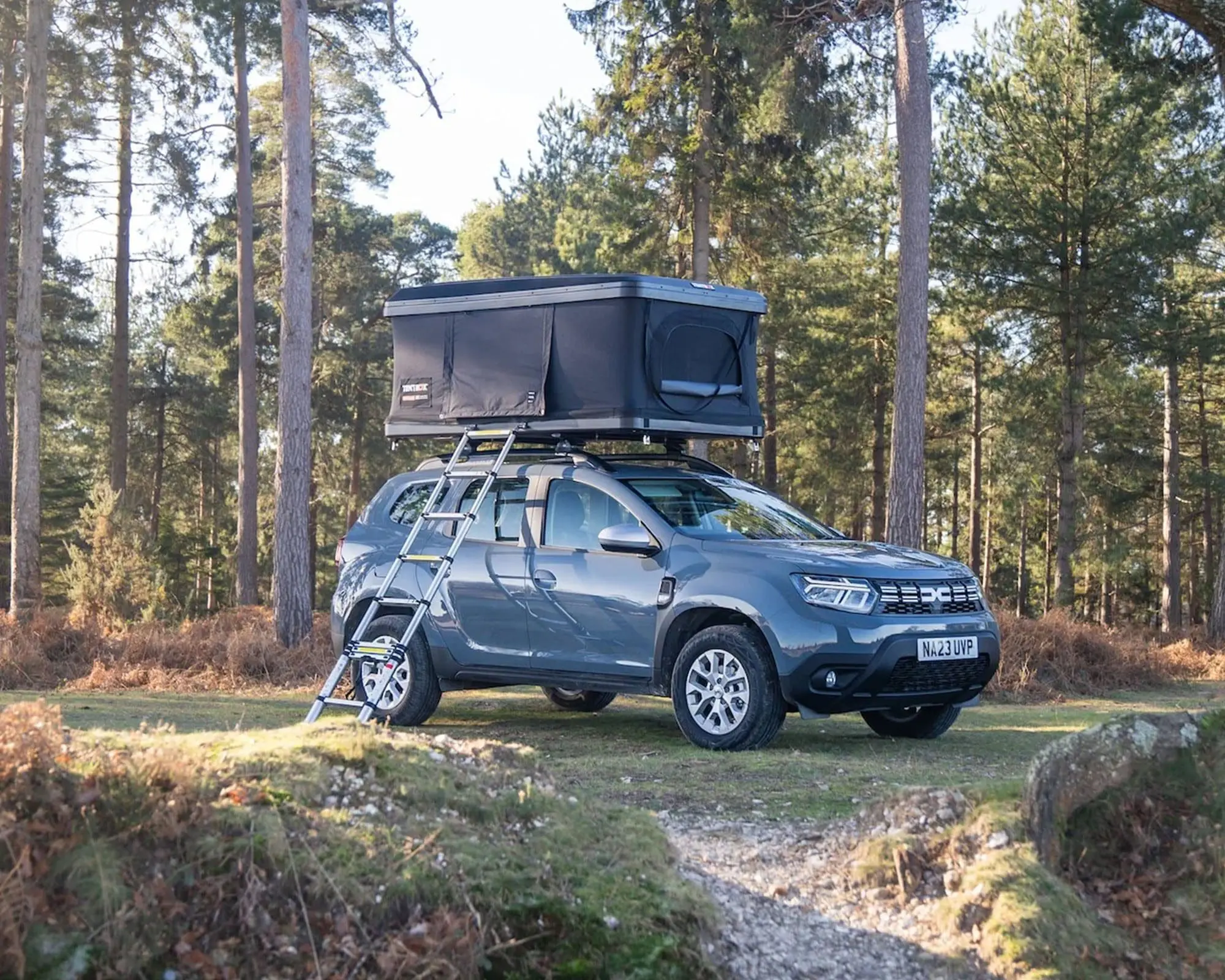 Outdoor scene featuring a gray SUV equipped with a rooftop tent parked on a forested trail