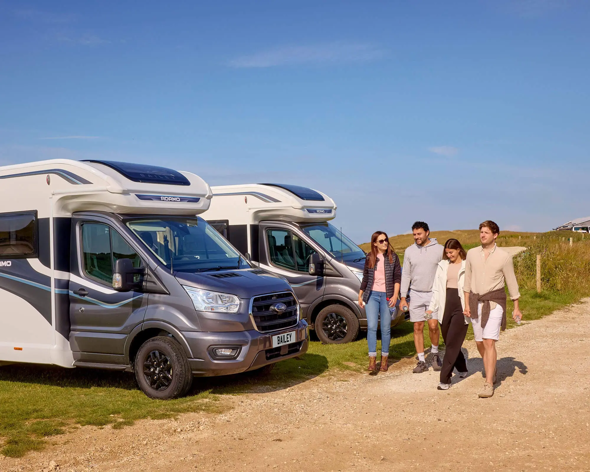 Four friends walking beside two campervans on a sunny day, surrounded by nature.
