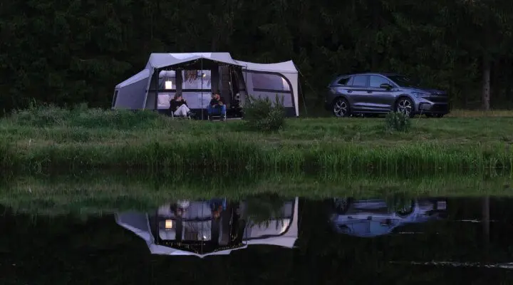 A cozy camping setup featuring a caravan and a vehicle by a tranquil lake, showcasing a perfect outdoor escape.