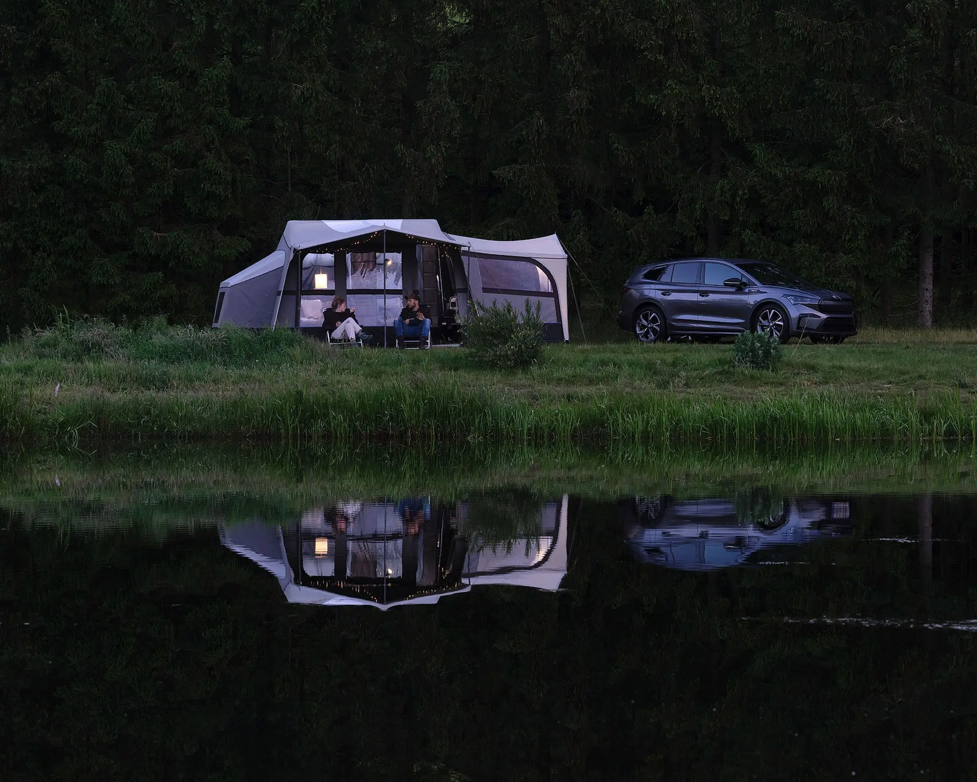 A cozy camping setup featuring a caravan and a vehicle by a tranquil lake, showcasing a perfect outdoor escape.
