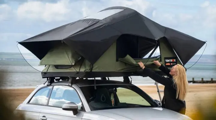 Person setting up a TentBox rooftop tent on a car near a beach, showcasing innovative camping solutions for adventurers.
