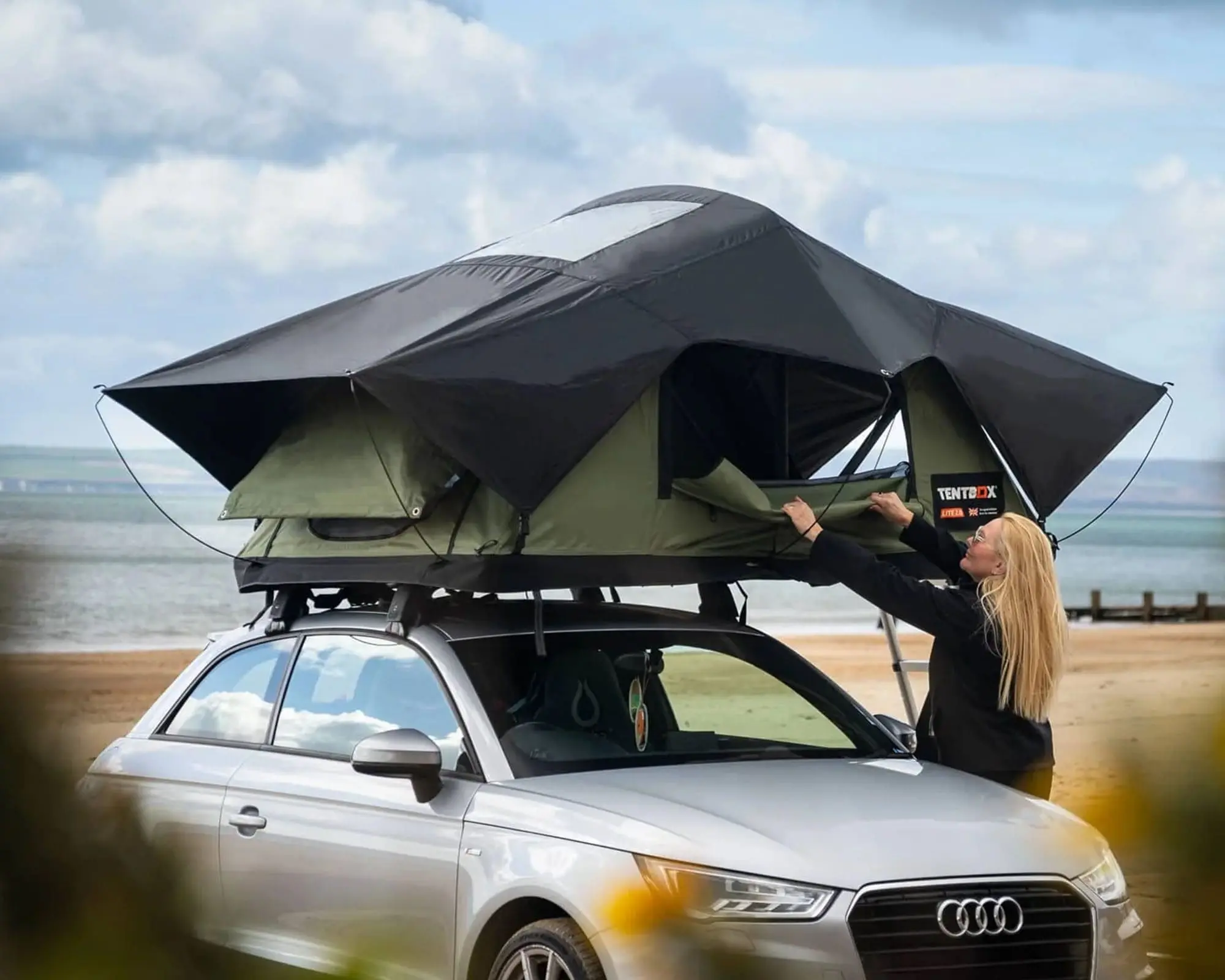 Person setting up a TentBox rooftop tent on a car near a beach, showcasing innovative camping solutions for adventurers.