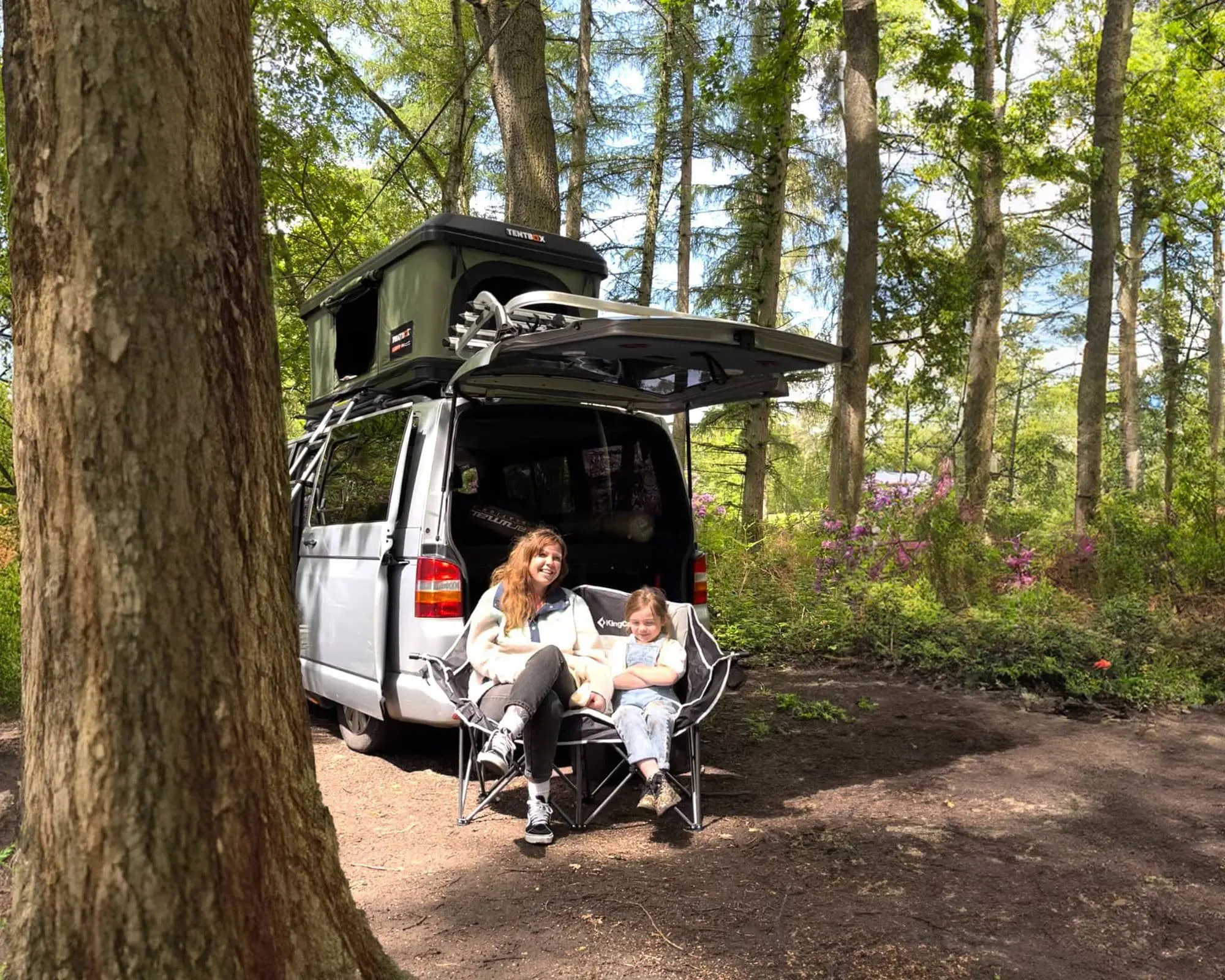 A woman and child enjoying their time by a campervan equipped with a TentBox in a peaceful forest.