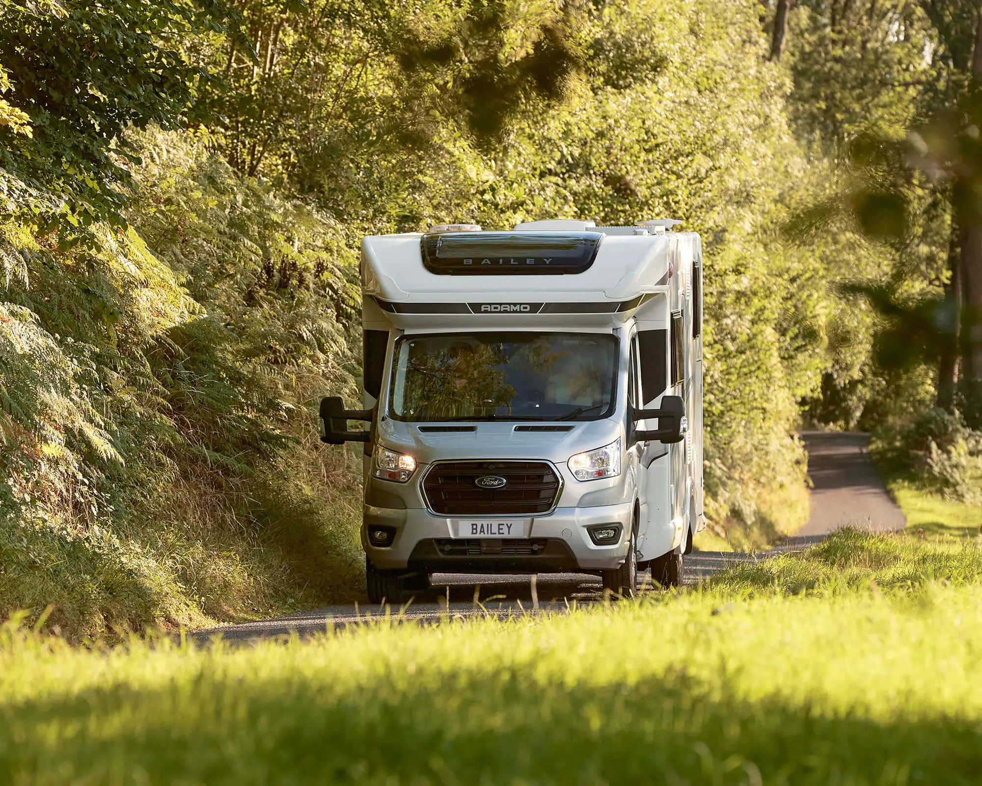 A Bailey motorhome navigating a tree-lined country road, showcasing its design and features in a natural setting.