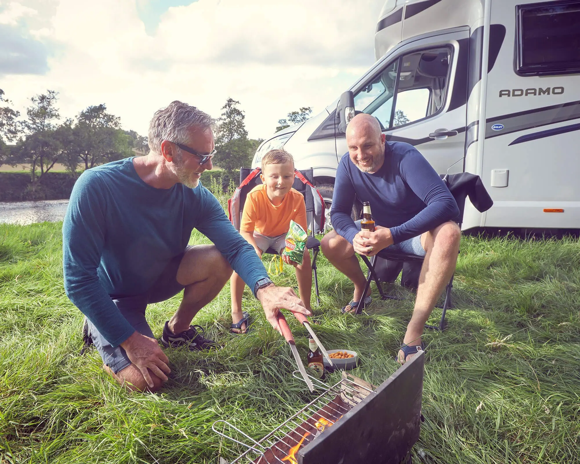 A family grilling outdoors near a Bailey motorhome, enjoying a camping experience.