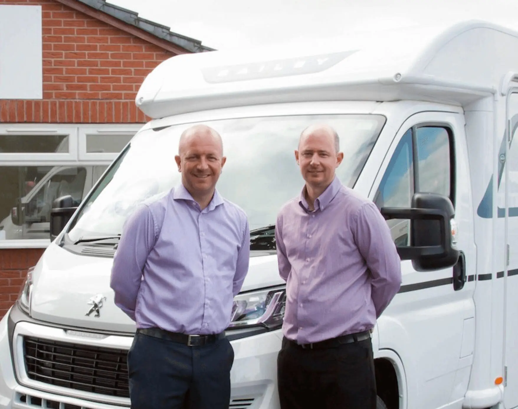 Two professionals standing in front of a Bailey motorhome, ready to assist customers with their caravan and campervan needs.