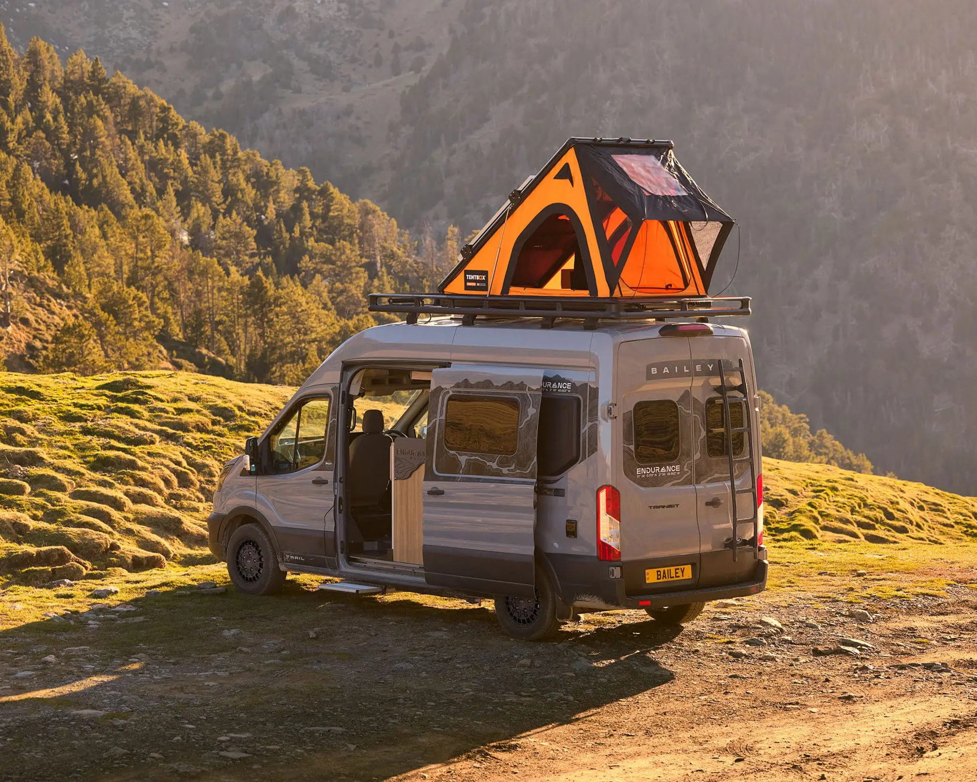 A camper van parked in a lush mountainous area with a rooftop tent setup, ideal for outdoor adventures.