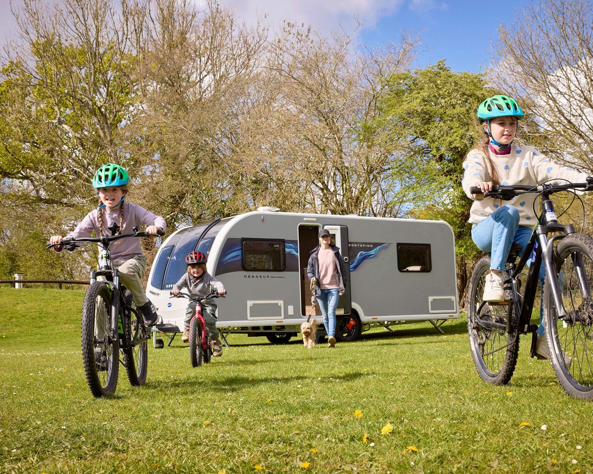 A family bikes around their Bailey caravan in a scenic outdoor setting, showcasing camping and outdoor fun.