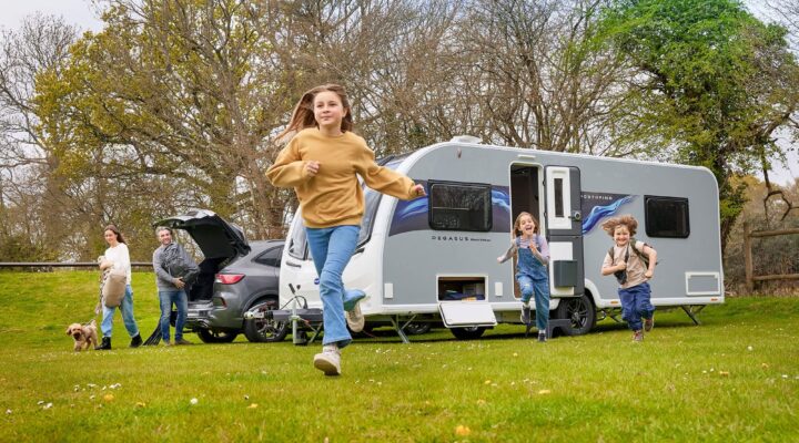 A family with children and a dog playing outside their Bailey caravan in a scenic green area.