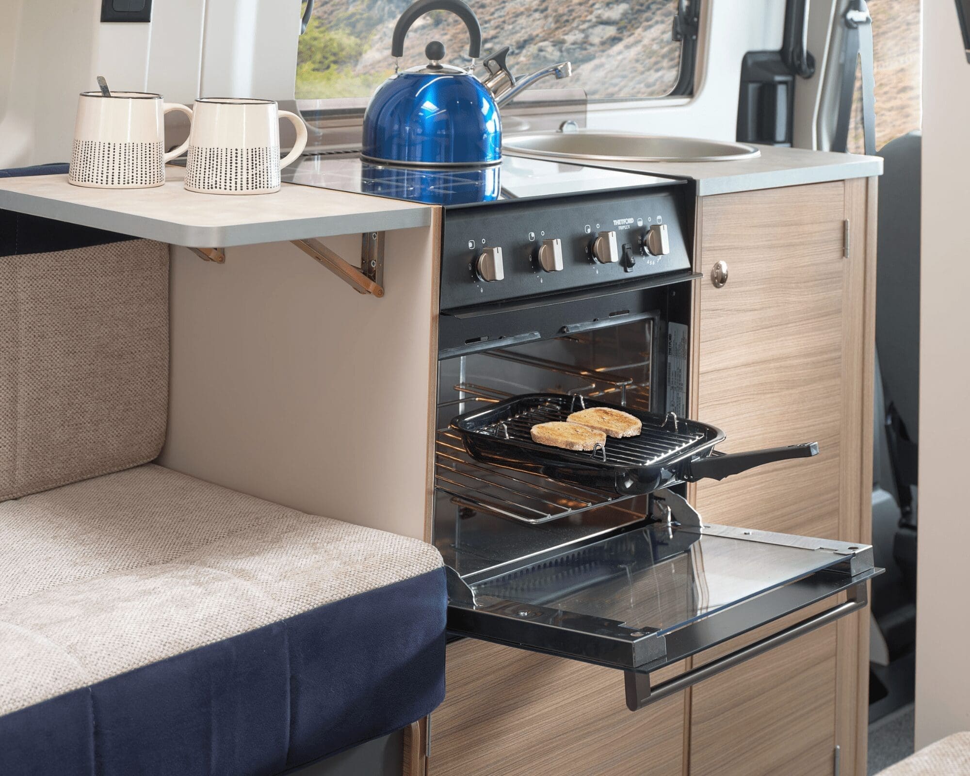 Modern Caravan Kitchen with Oven and Blue Kettle Interior of a caravan kitchen featuring an oven, a blue kettle, and a cozy seating area.