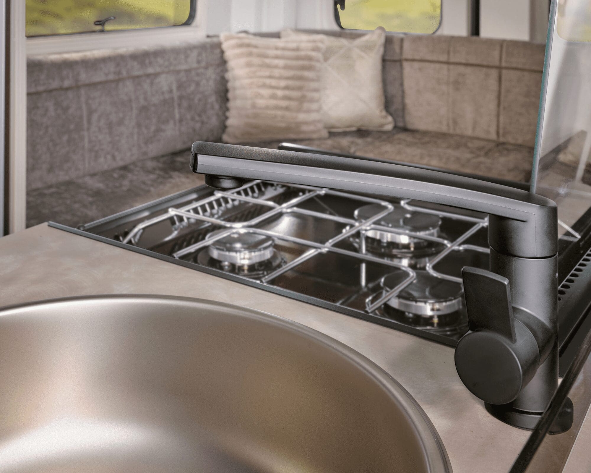 Modern Kitchen Setup in Bailey Caravan Interior view of a Bailey caravan kitchen featuring a sink and stove, with cozy seating in the background.