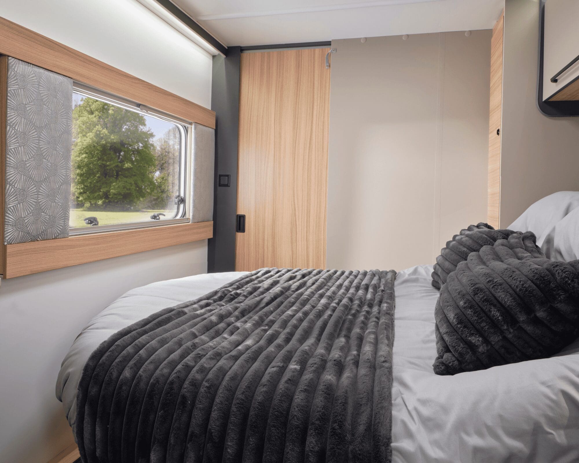 A comfortable caravan bedroom featuring a double bed with plush bedding and a window that offers a glimpse of the outdoors.