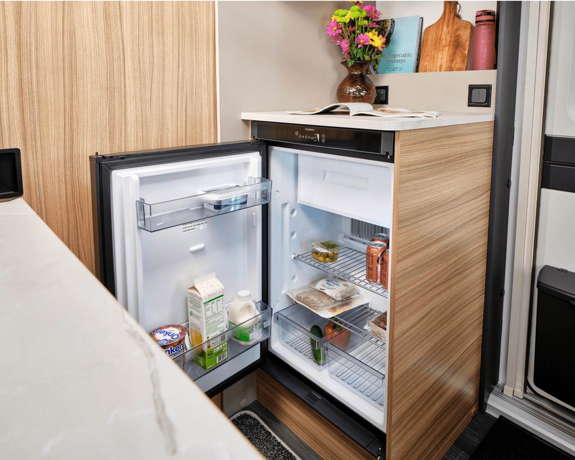 Open fridge in a Bailey caravan showcasing organized food storage and interior design.