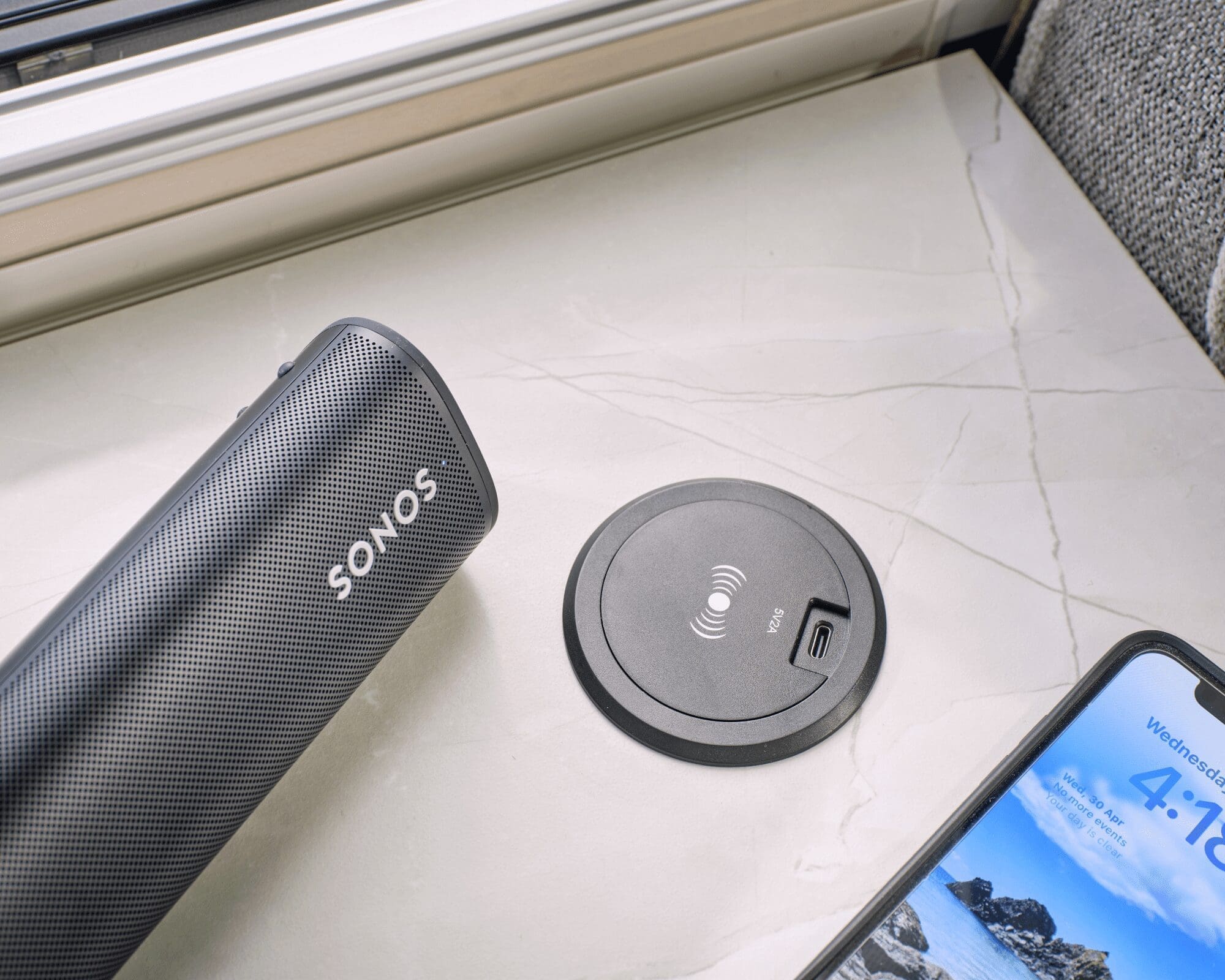 A Sonos portable speaker next to a charging station and a smartphone on a countertop inside a caravan.