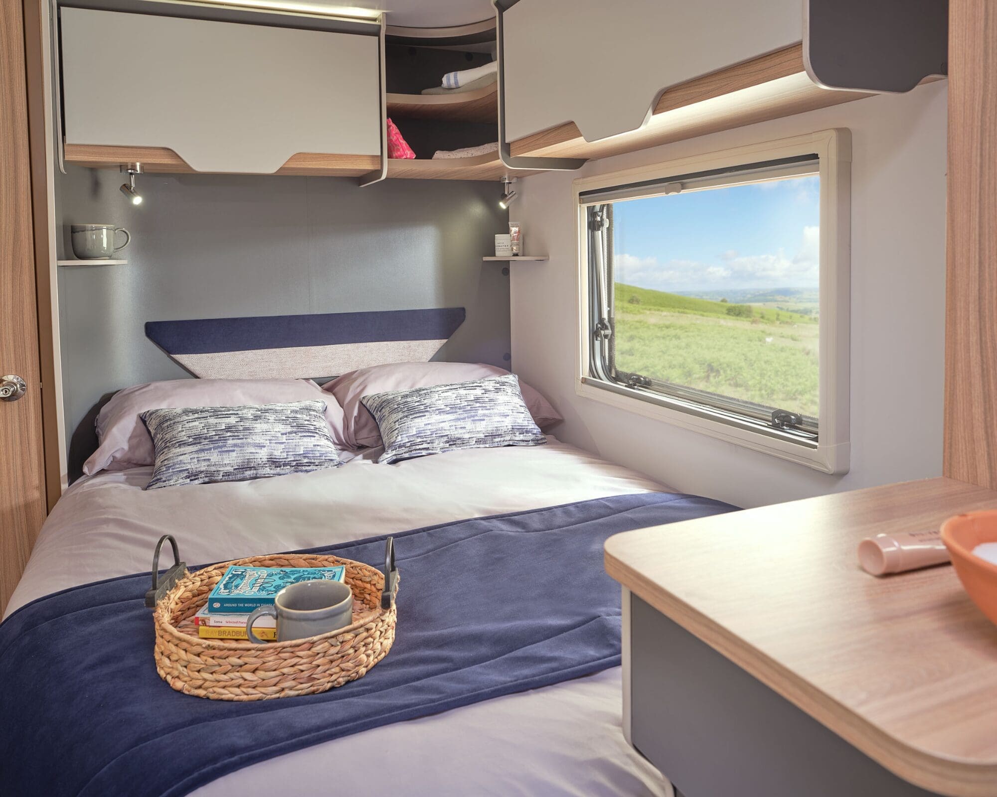 Bed area inside a Bailey caravan featuring soft bedding and a window overlooking a serene landscape.