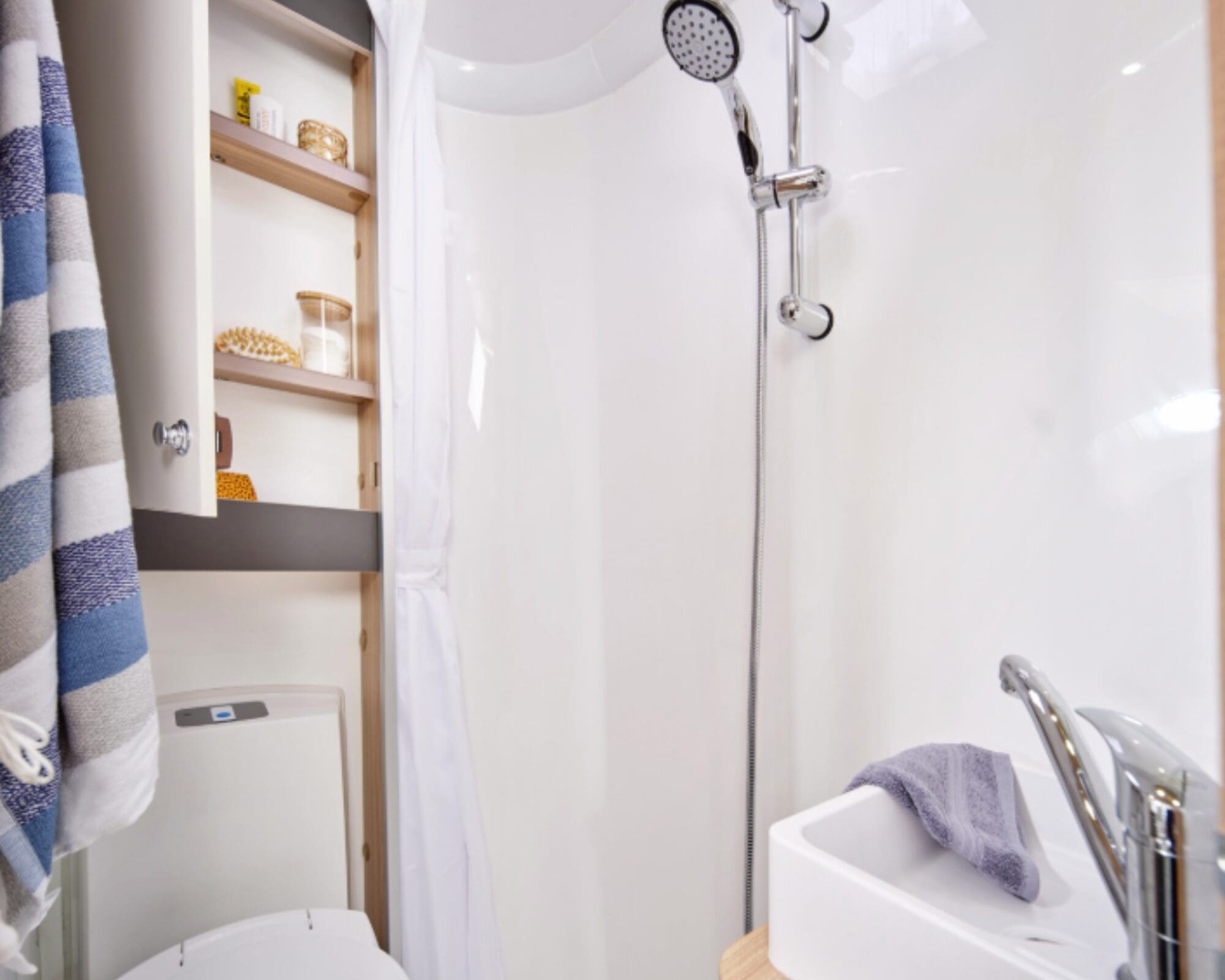Interior view of a compact shower room in a caravan, showcasing a shower, sink, and storage shelves.