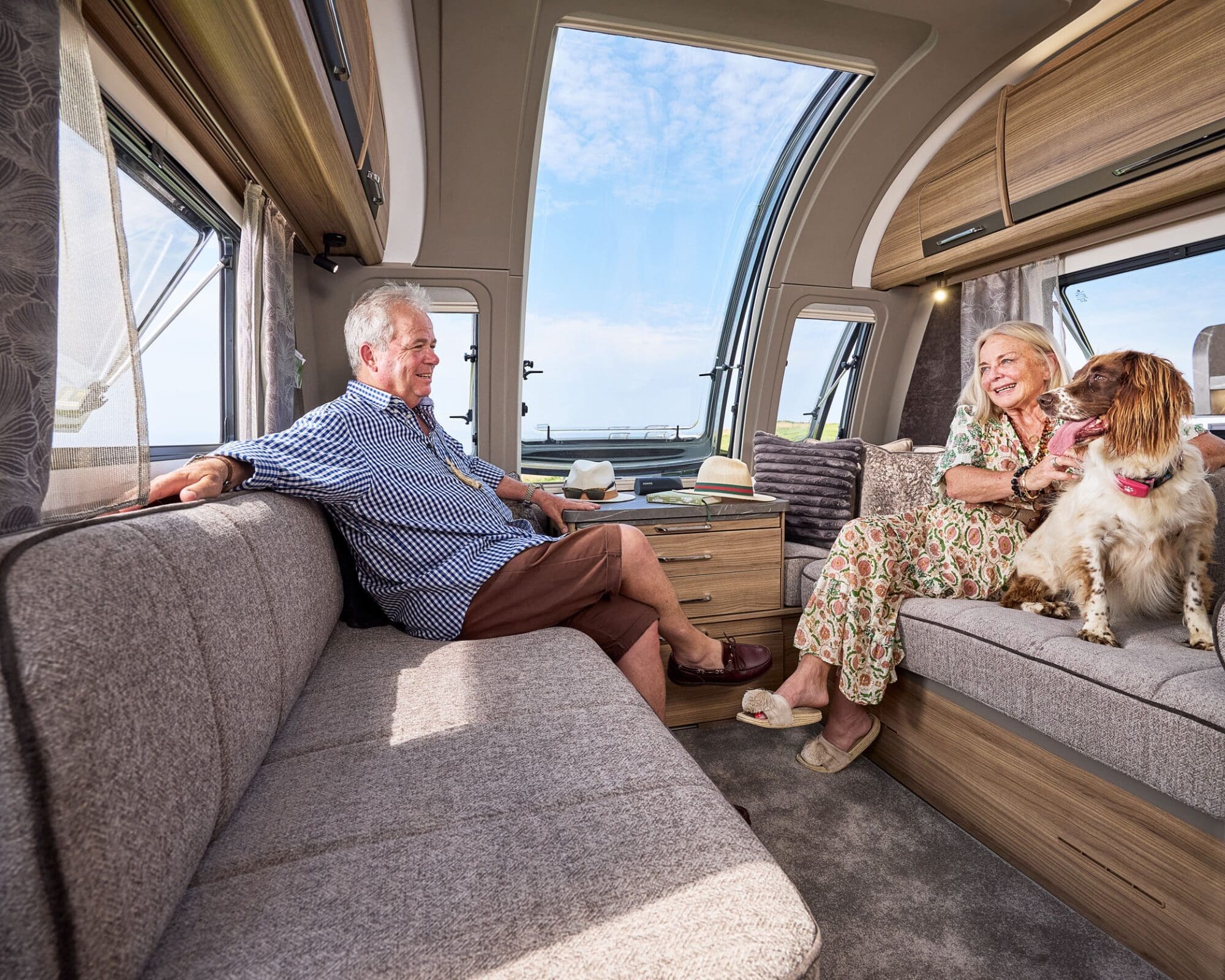 Interior view of a Bailey caravan featuring a couple relaxing on a sofa with their dog, showcasing a spacious and comfortable living area.