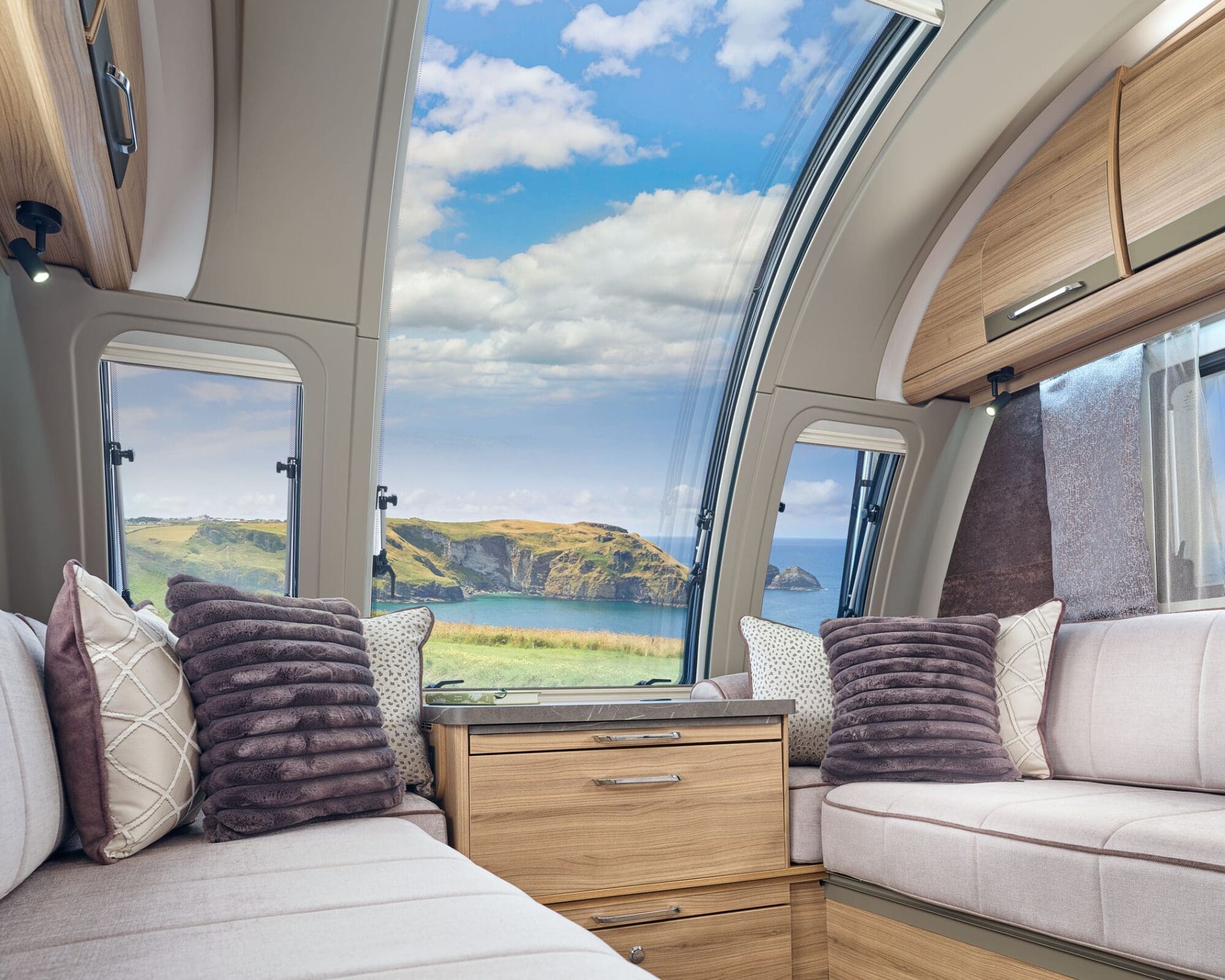 Cozy seating area inside a Bailey motorhome featuring large windows with a stunning coastal view.