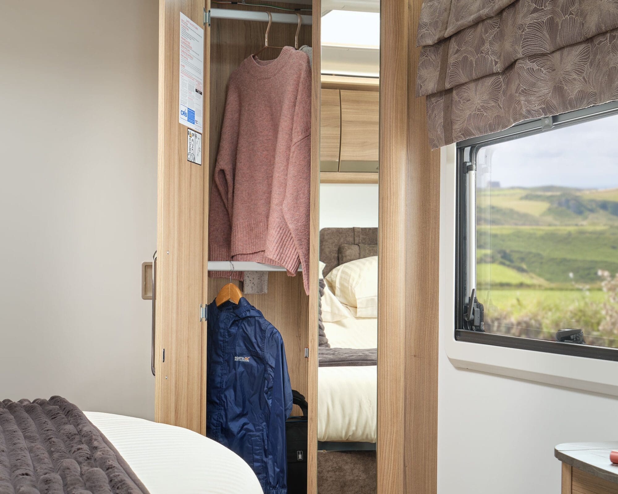Wardrobe area showcasing clothing in a Bailey caravan with scenic view outside the window.