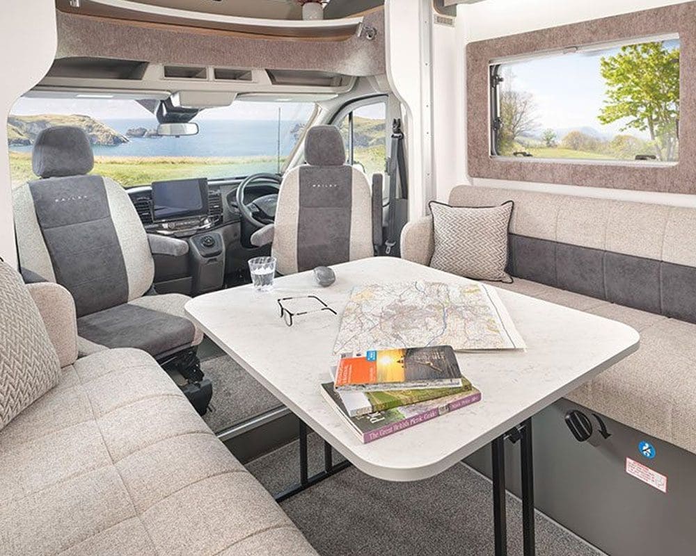 Interior view of a Bailey motorhome featuring a spacious seating area, a table, and scenic views through the windows.